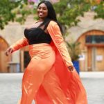 Olakemi - A curvy plus size model wearing a plus size black top and plus size orange pants and jacket