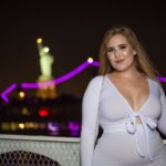 Plus Size Model Sophie Turner wearing a plus size white outfit in front of the Statue of Liberty in NYC
