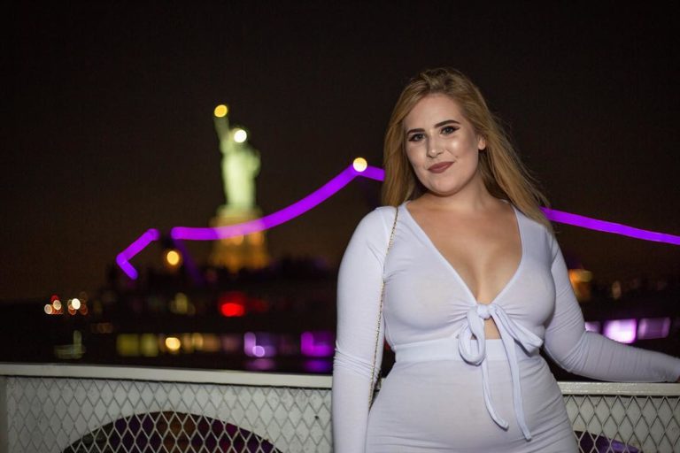 Plus Size Model Sophie Turner wearing a plus size white outfit in front of the Statue of Liberty in NYC